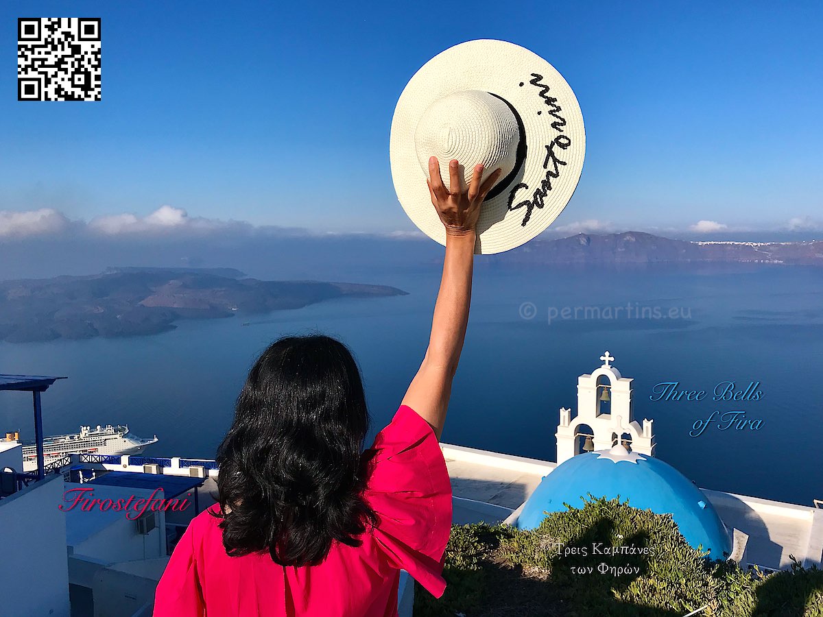 Greece Santorini Firostefani women in red holding a hat text "Santorini" at the church Three Bells of Thira view over caldera
